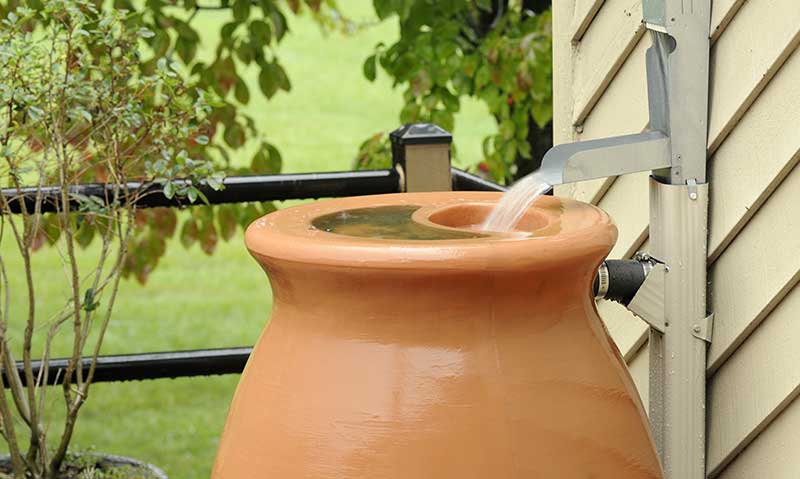 Terracotta rain barrel catching water during a storm